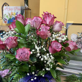 Pink roses arranged in a glass vase with white baby's breath and purple ribbon