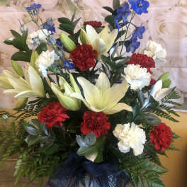 Arrangement of white lilies, red and white carnations, and blue delphinium in a vase