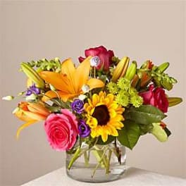 Mixed bouquet of lilies, roses, and a sunflower in a clear glass vase