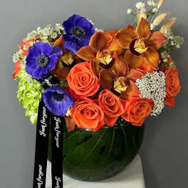 Orange roses and blue anemones in a glass vase with black ribbons