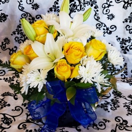 Yellow roses and white lilies in a bouquet with a blue ribbon