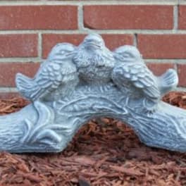 Decorative stone bird sculpture on mulch in front of a brick wall