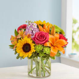 Colorful bouquet in a clear glass vase with a sunflower, rose, lilies, and mixed blooms