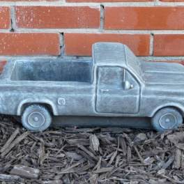 Gray pickup truck-shaped planter on mulch in front of a brick wall