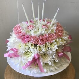 Round pink and white floral cake with tall white candles on a plate