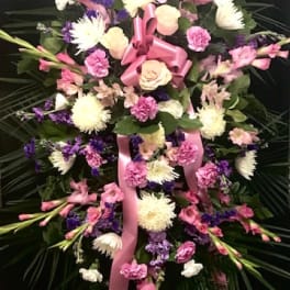 Large pink and white floral standing spray with ribbon on a dark backdrop