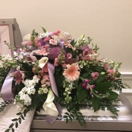 Large pastel floral arrangement with ribbons on a casket