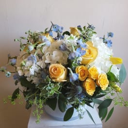 Bouquet of yellow roses, white hydrangeas, and blue flowers in a white vase