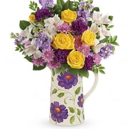 Bouquet of yellow roses, purple flowers, and white lilies in a floral pitcher vase