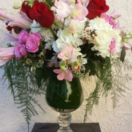 Mixed bouquet of red roses, pink orchids, and white hydrangeas in a glass vase