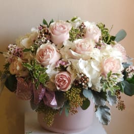Blush roses and white flowers in a pink vase with a ribbon