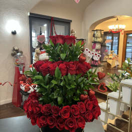 Tiered arrangement of red roses with heart decorations in a black round box