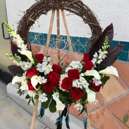 Floral wreath with red roses, white calla lilies, and white blossoms on an easel