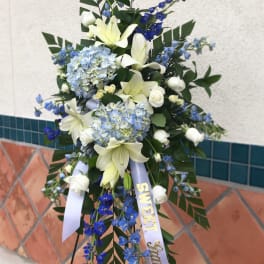 Standing floral spray with white lilies, blue hydrangeas, and blue delphinium