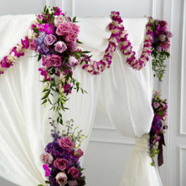 Purple and pink floral garland draped over a white wedding arch