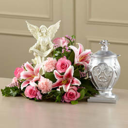 Pink lilies and roses arranged beside an angel figurine and silver urn