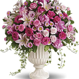 Large pink and lavender flower arrangement with lilies and roses in a white pedestal urn