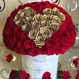 Round box arrangement of red roses with a heart of gold roses on a reflective surface