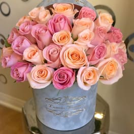 Round hat box of pink and peach roses arranged tightly together