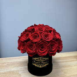 Dome of red roses arranged in a black round hat box on a wooden table.