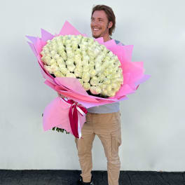 Man holding an oversized bouquet of white roses wrapped in bright pink paper