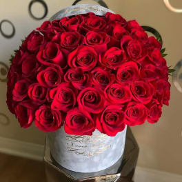 Round hatbox filled with tightly packed red roses on a reflective pedestal