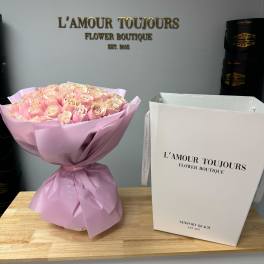 Pink rose bouquet wrapped in pale pink paper next to a tall white gift box.