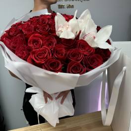 Large bouquet of red roses with white orchids wrapped in white paper, held by a person indoors