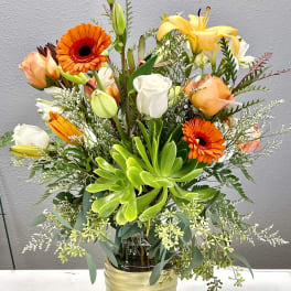 Mixed bouquet with orange gerberas, lilies, and roses in a glass vase
