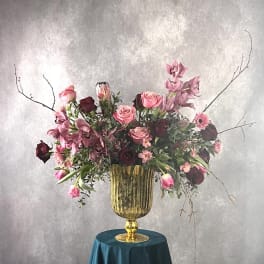 Large pink and burgundy floral arrangement in a gold urn vase