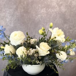White roses and blue flowers arranged in a white bowl vase