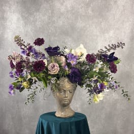 Purple and white floral arrangement in a sculpted head vase