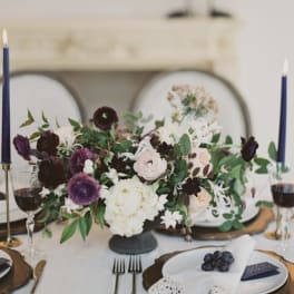 Low floral centerpiece with white, blush, and dark purple blooms on a dining table