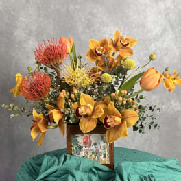 Orange and yellow floral arrangement in a wooden frame container