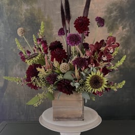 Tall floral arrangement in a wooden box with burgundy and purple blooms