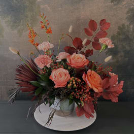 Arrangement of peach roses, pink carnations, and orange blooms in a vase