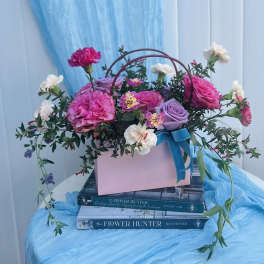 Pink and lavender roses with small white blooms in a pink box with a blue ribbon