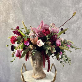 Large floral arrangement in a sculpted bust vase with pink and burgundy blooms