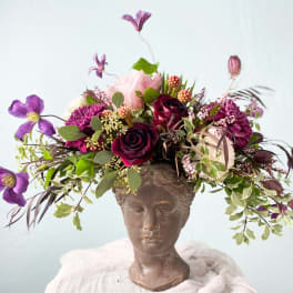 Floral arrangement in a sculpted head vase with purple and pink blooms