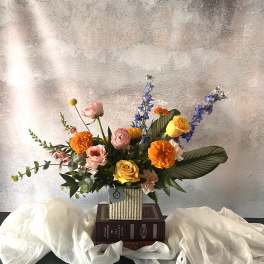 Colorful mixed flower arrangement in a striped vase on stacked books