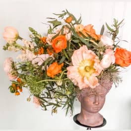 Orange and blush flowers arranged in a sculpted head vase