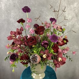 Large burgundy and pink floral arrangement in a white urn vase