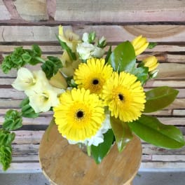 Yellow gerbera daisies and pale lilies in a glass vase