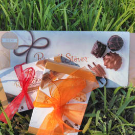 Three boxed chocolate assortments tied with red and orange ribbons on grass.