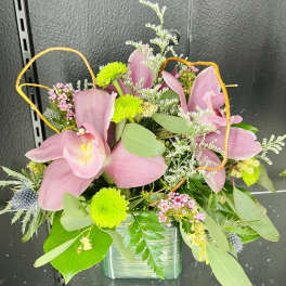 Compact arrangement of pink lilies and green button mums in a green glass cube vase