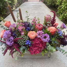Colorful floral arrangement in a wooden box with pink, purple, and burgundy blooms