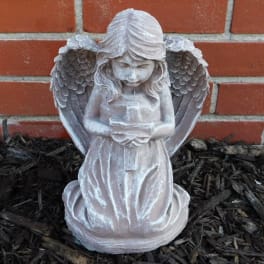 White angel statue holding a candle in front of a brick wall