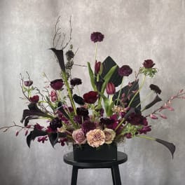 Tall floral arrangement with dark purple blooms in a black rectangular container