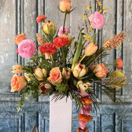 Tall floral arrangement in a white vase with pink, peach, and yellow blooms
