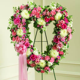 Heart-shaped floral wreath with pink roses and white blooms on a stand